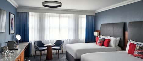 A hotel room with two beds, a desk, a chair, a desk lamp, and a window with curtains.