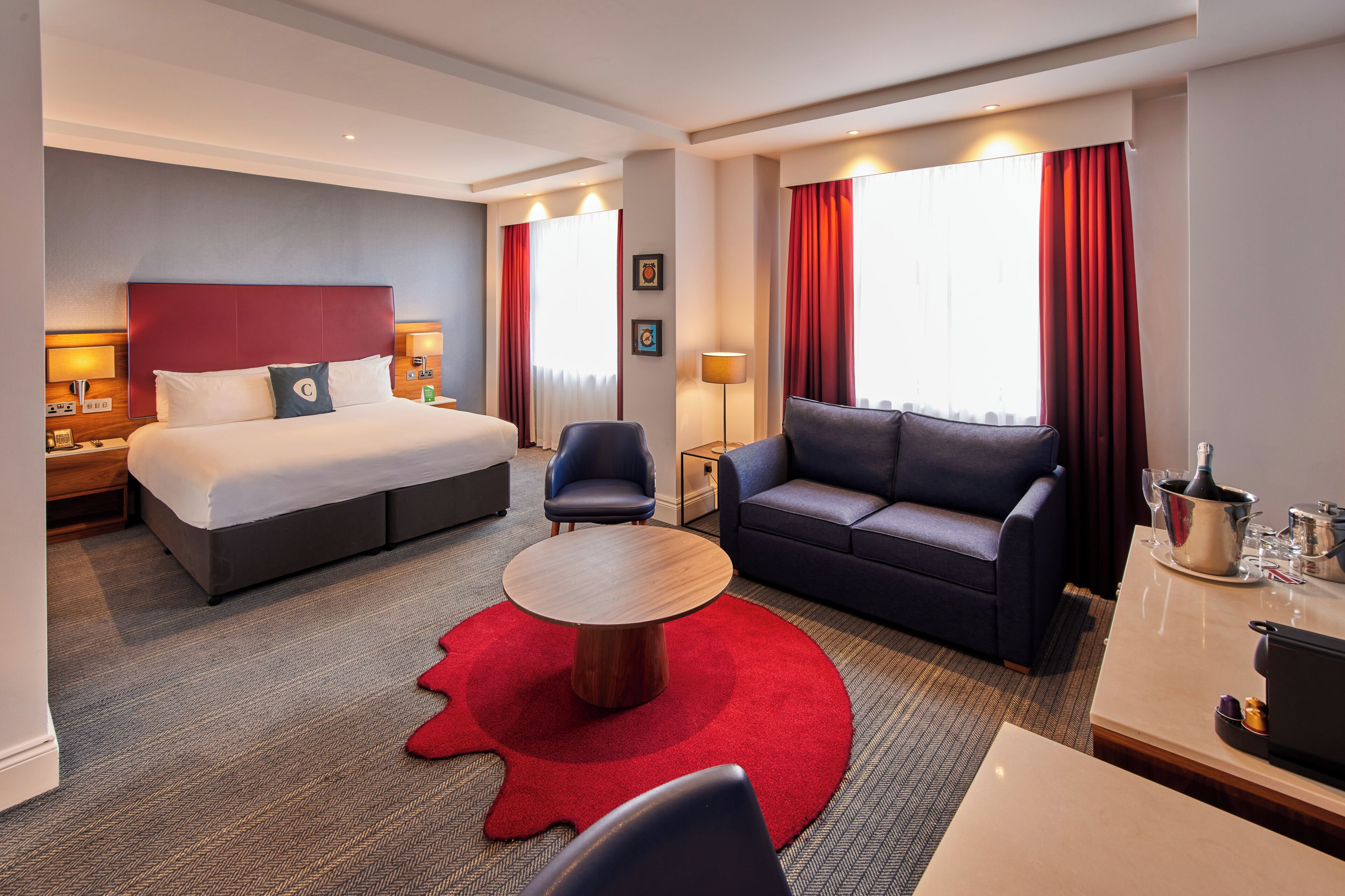Una habitación de hotel con una cama, un sofá, una mesa de centro y un escritorio con una lámpara.