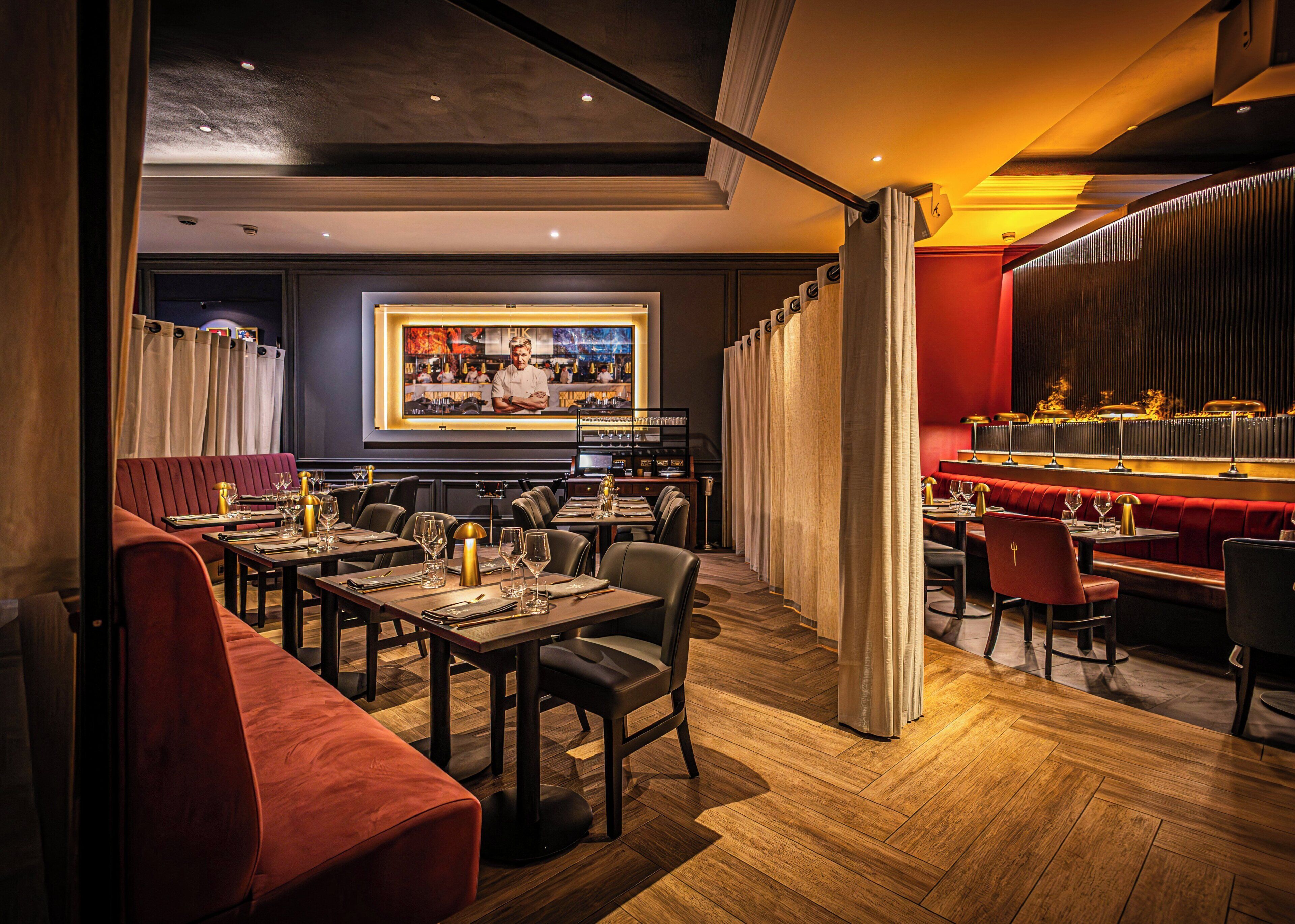A restaurant with wooden flooring, red upholstered seating, and a bar area with a television screen.