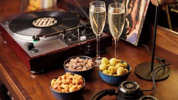 A turntable, two glasses of champagne, bowls of nuts and olives, and a pair of headphones on a wooden table.