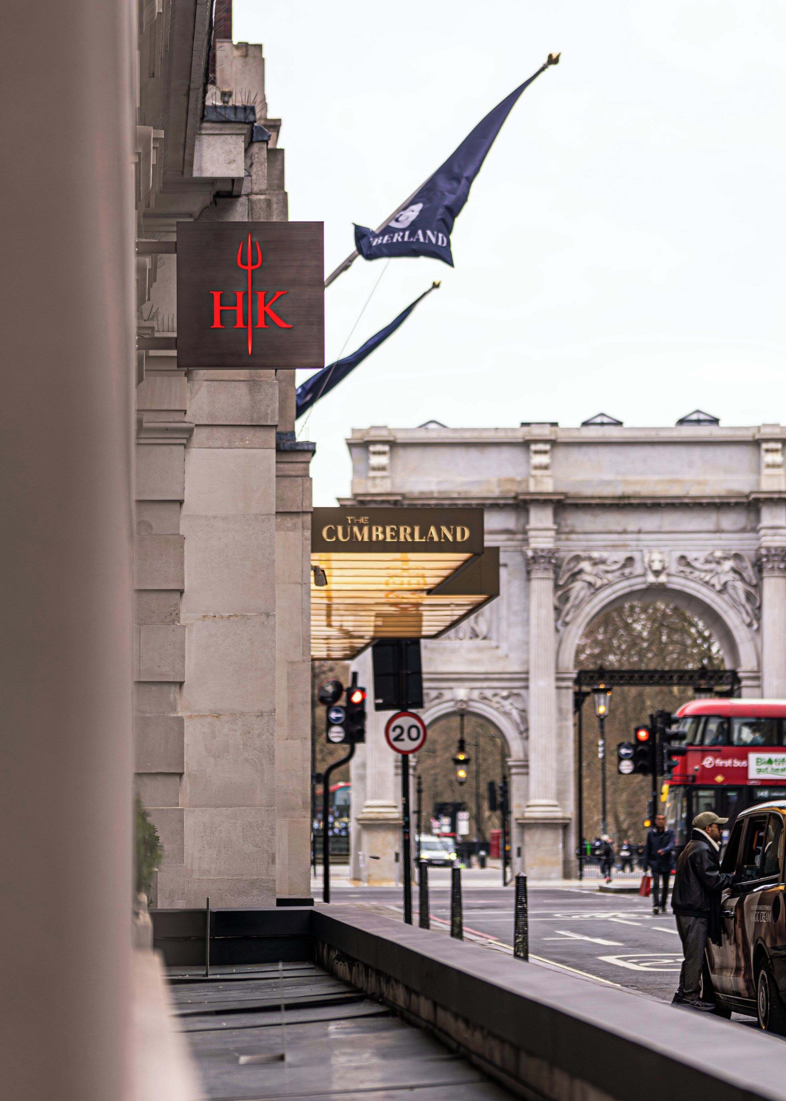 Entrada de un hotel con un cartel que dice 'The Cumberland' y una bandera de 'HIK'.