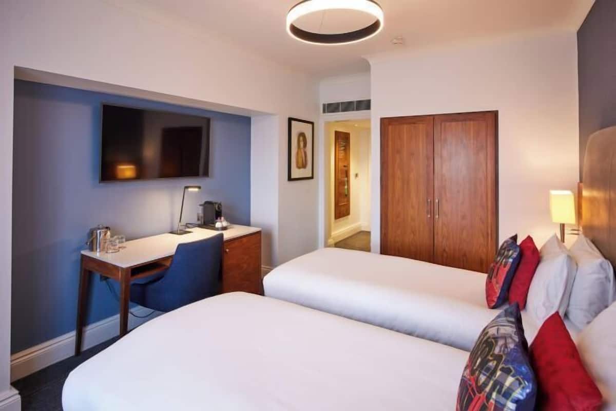 Hotellihuone, jossa on kaksi sänkyä, työpöytä, tuoli, televisio ja vaatekaappi.