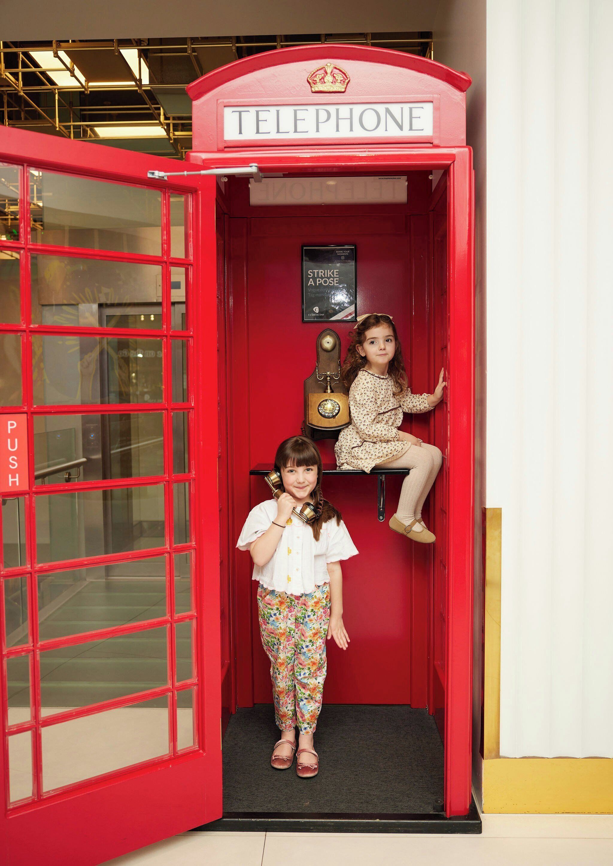 A red telephone booth with a sign reading 'TELEPHONE' and a small shelf with a guitar.