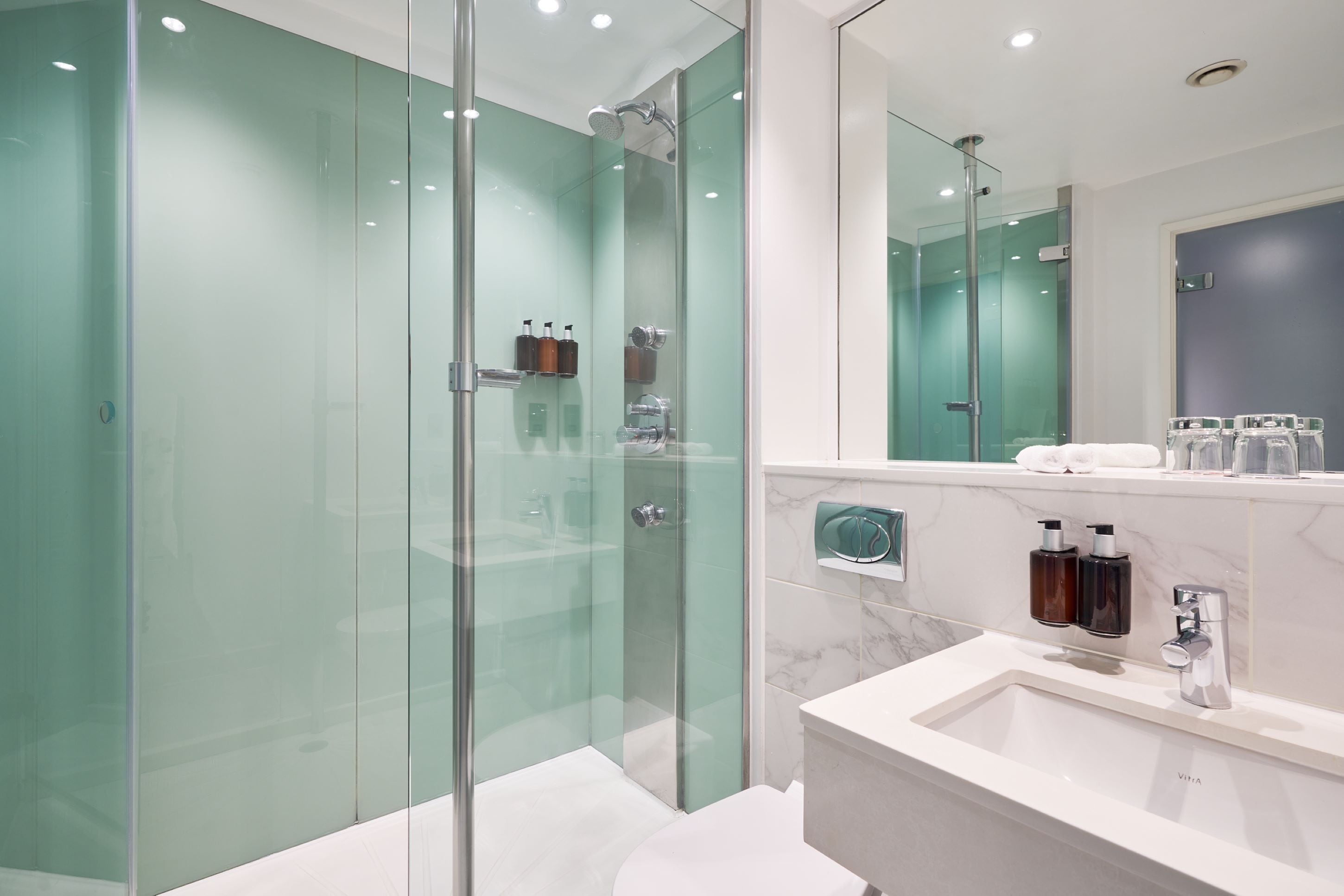 Un baño moderno con ducha envuelta en vidrio, un lavabo blanco y un salpicadero de mármol.