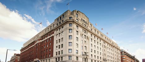 Un edificio grande e histórico con varios pisos, una entrada destacada en esquina y banderas en la parte superior.