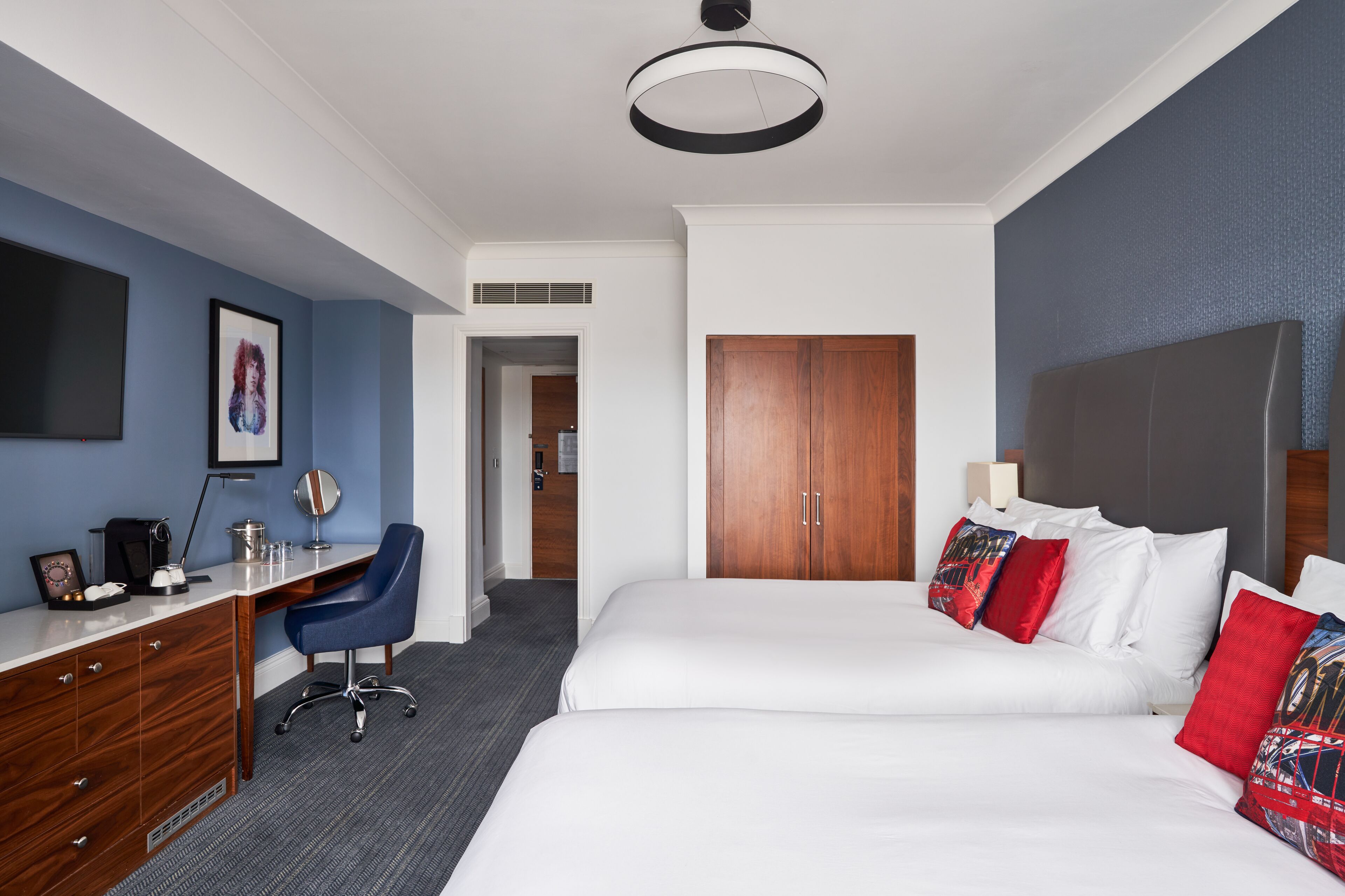 A hotel room with a desk, two beds, a wardrobe, and a large mirror.