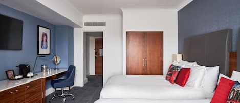 Una camera d'albergo con una scrivania, due letti, un armadio e uno specchio grande.