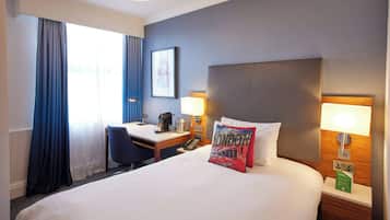 A hotel room with a bed, desk, chair, lamps, and a framed picture on the wall.