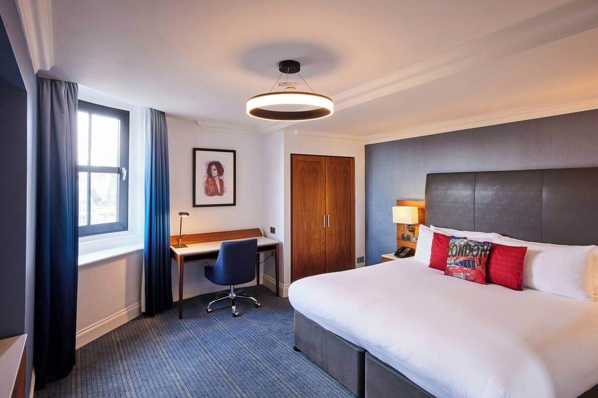 Ein Hotelzimmer mit einem großen Bett, einem Schreibtisch, einem Stuhl, einem Kleiderschrank und einem Bild an der Wand.