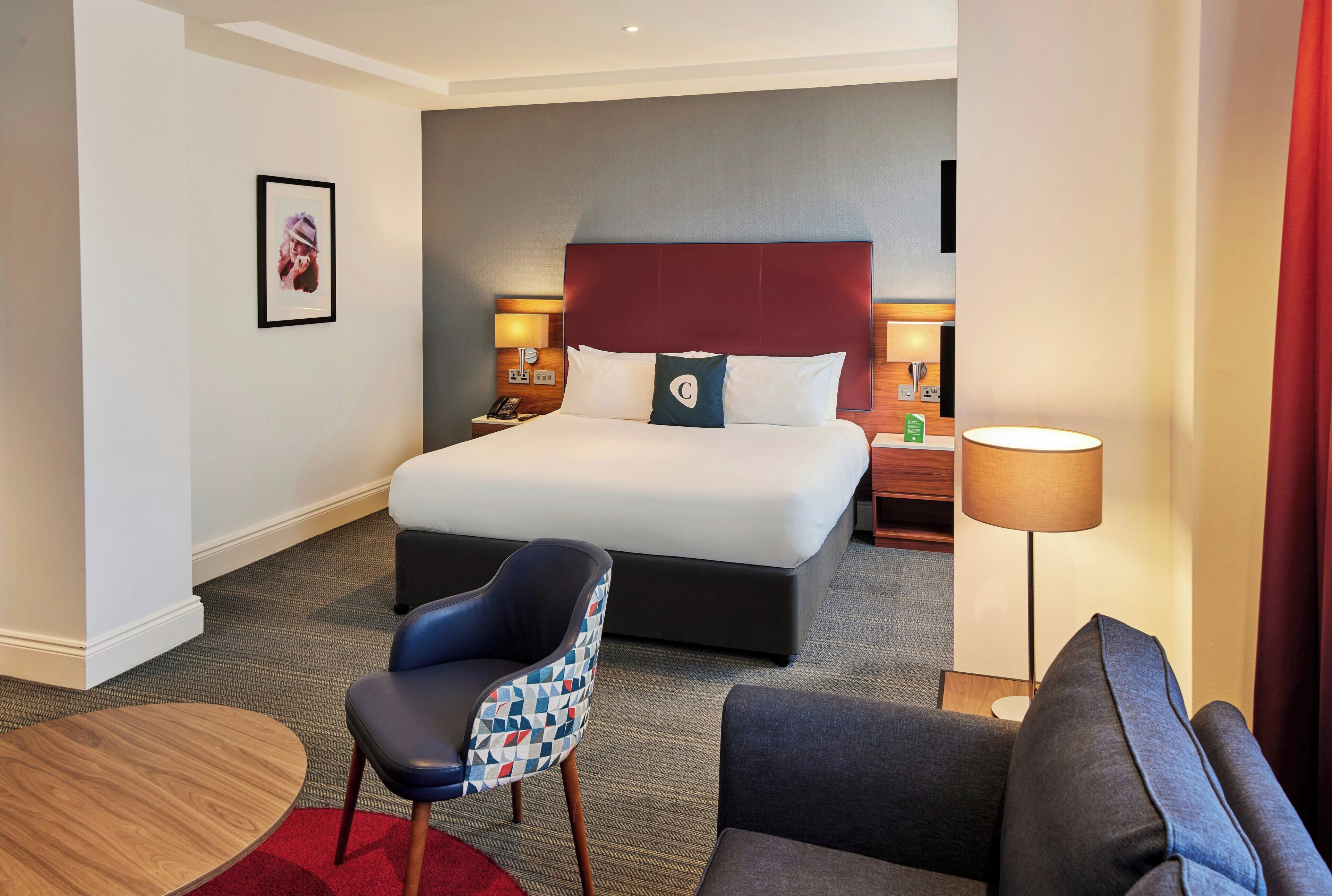 A hotel room with a large bed, two bedside tables, a desk, a chair, and a lamp.