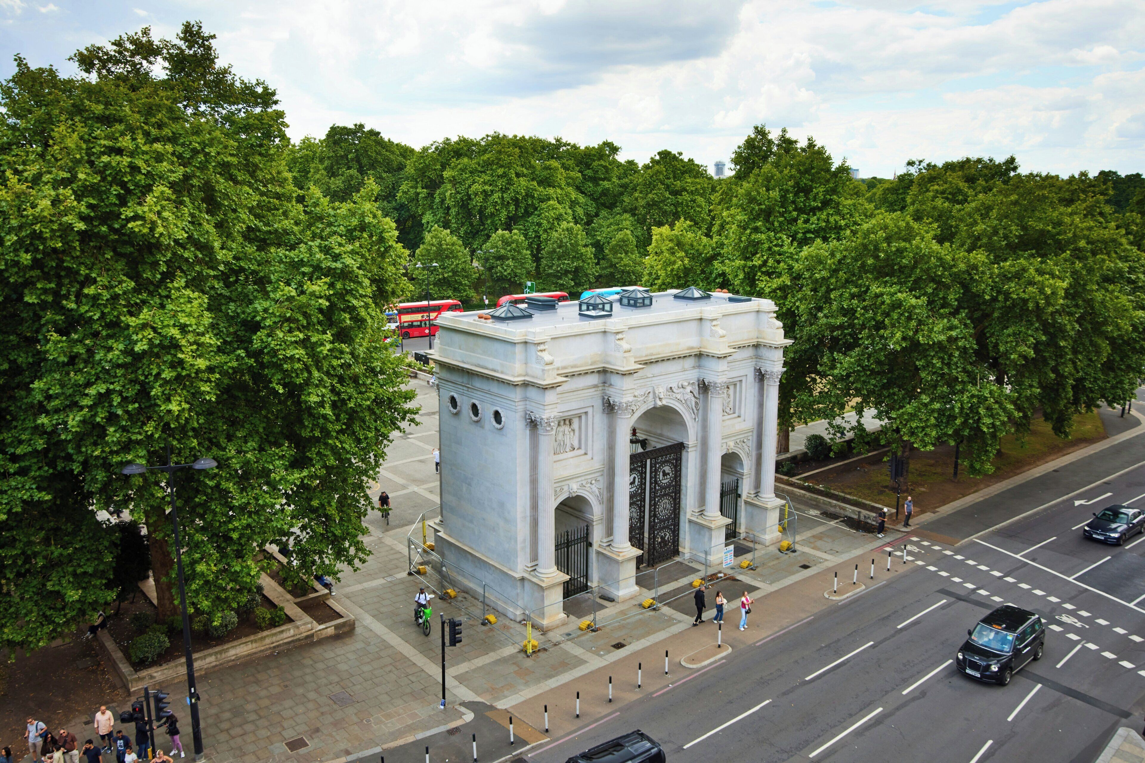 A large, ornate building with a prominent archway, surrounded by lush green trees.