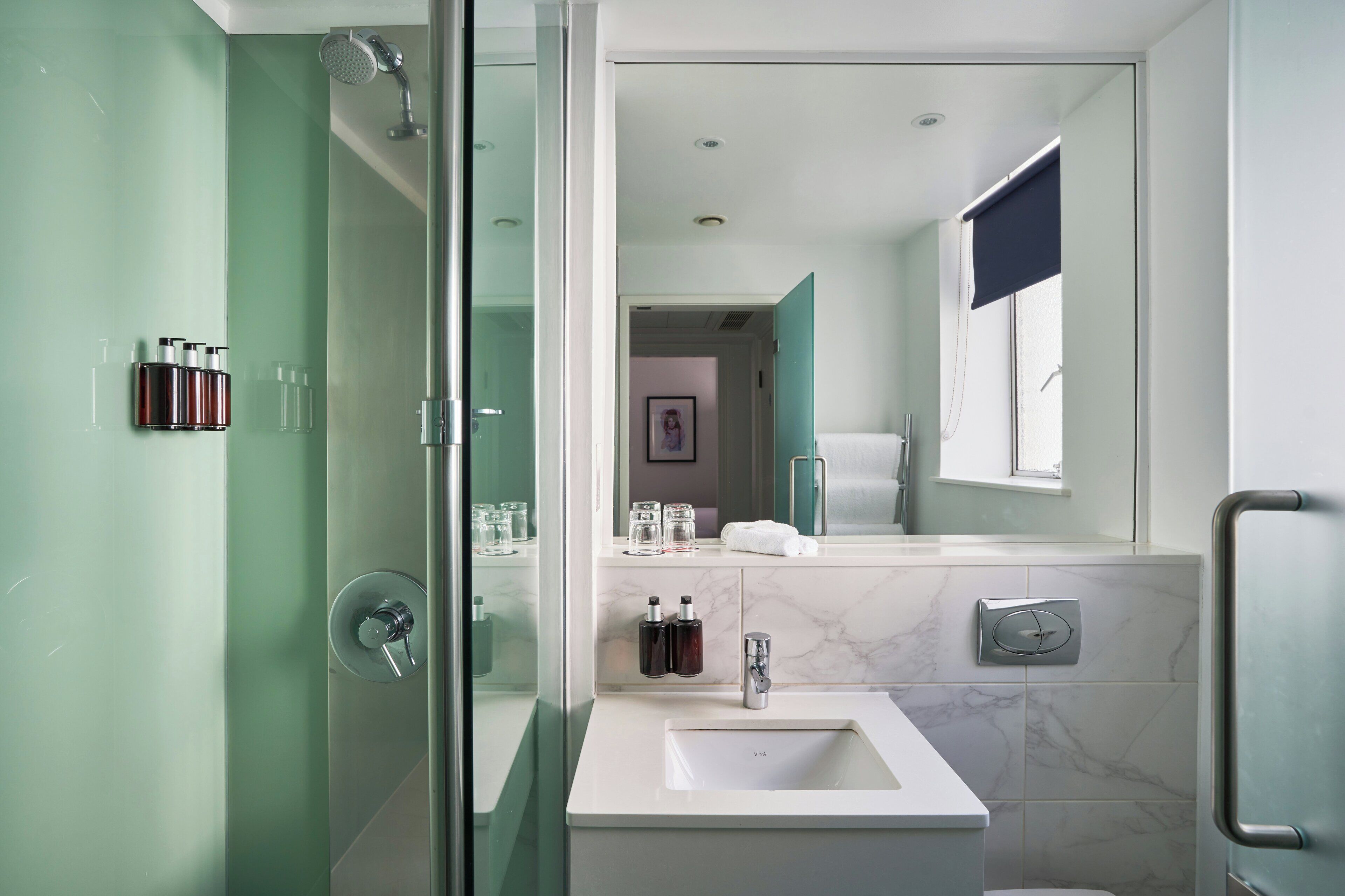 A modern bathroom with a glass shower enclosure, a white sink, and a marble backsplash.