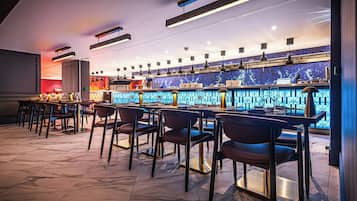 A bar area with multiple tables and chairs, a counter with a blue patterned backsplash, and overhead lighting fixtures.