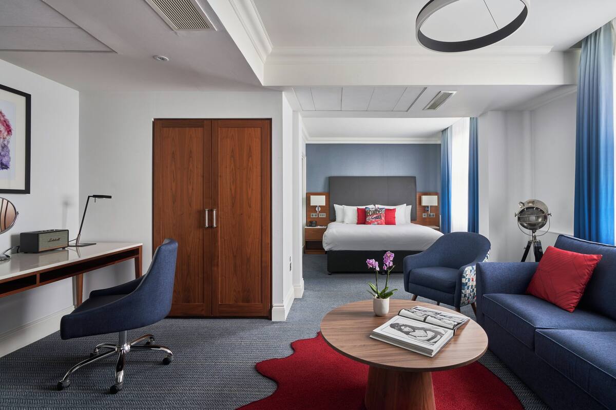 Ein Hotelzimmer mit Schreibtisch, Stuhl, Sofa und einem Bett mit Kopfteil.