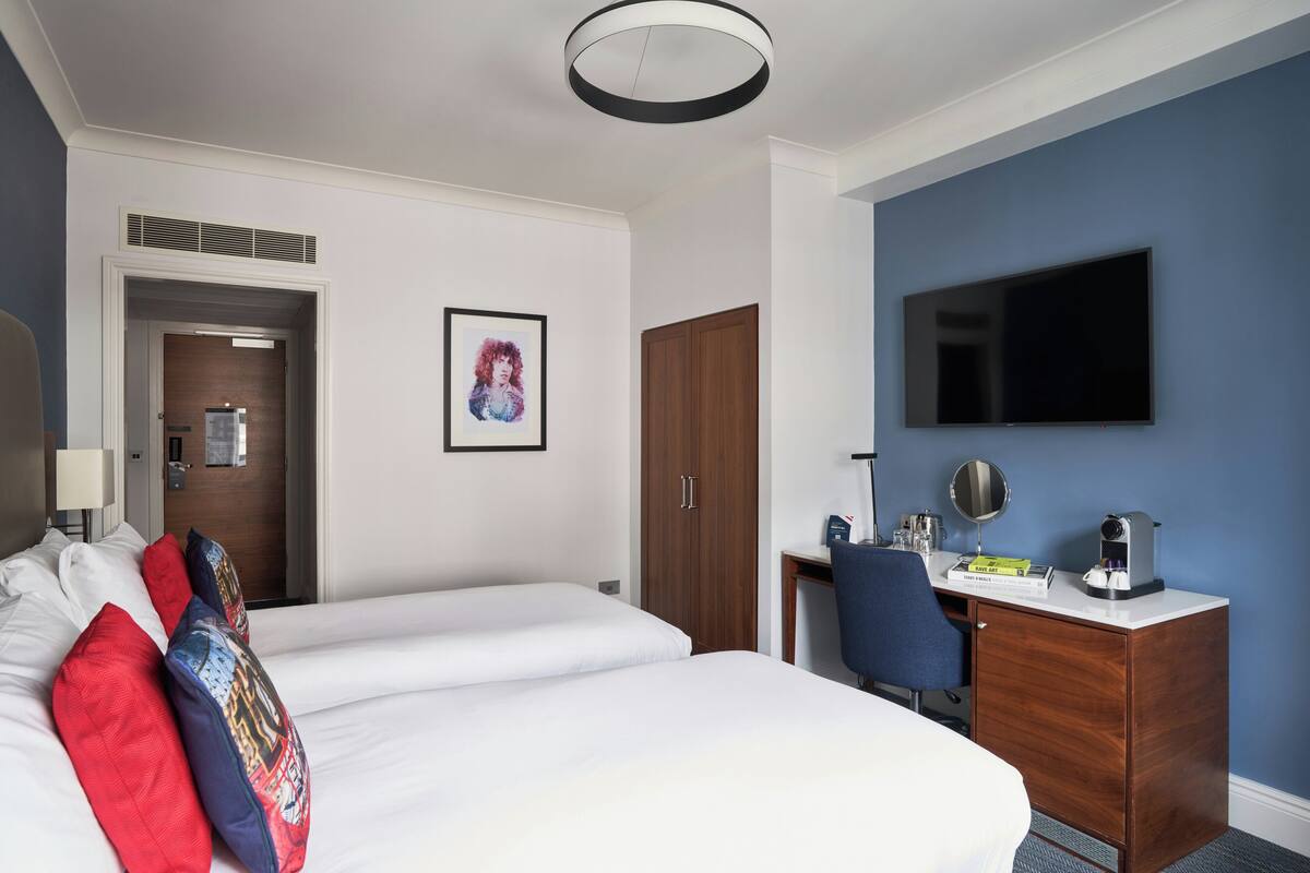 Hotellihuone, jossa on suuri sänky, työpöytä, tuoli, televisio ja ovi, joka johtaa toiseen huoneeseen.