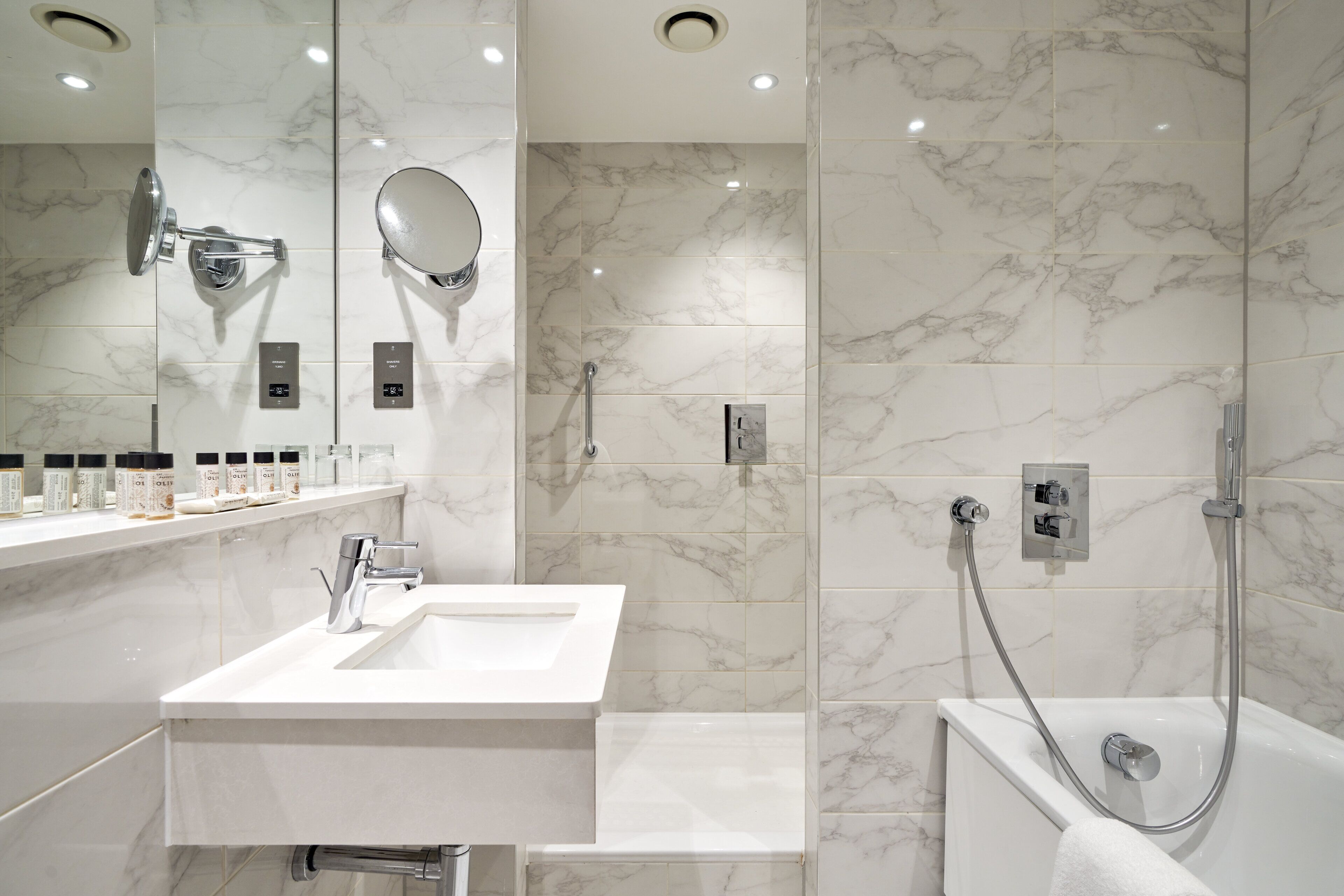 A modern bathroom with two sinks, a large mirror, and a walk-in shower.