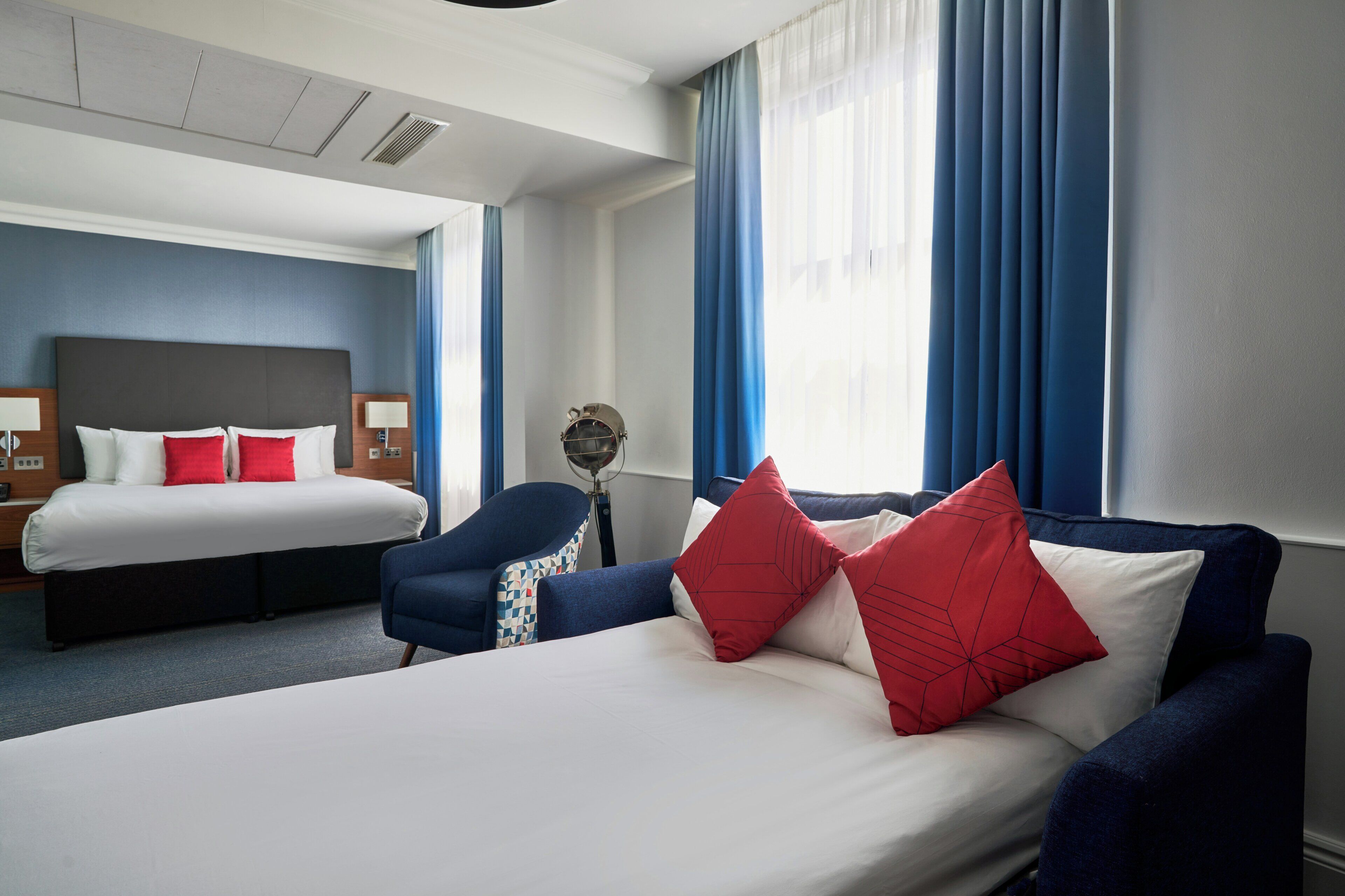 A hotel room with a bed, a sofa, a chair, and a lamp.