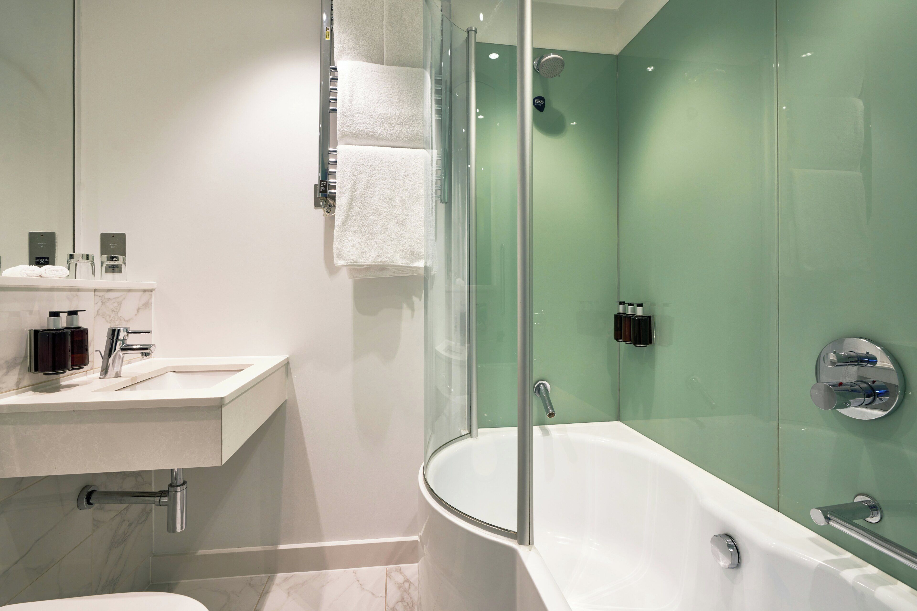 A modern bathroom with a glass-enclosed shower, a white bathtub, and a marble-tiled vanity.