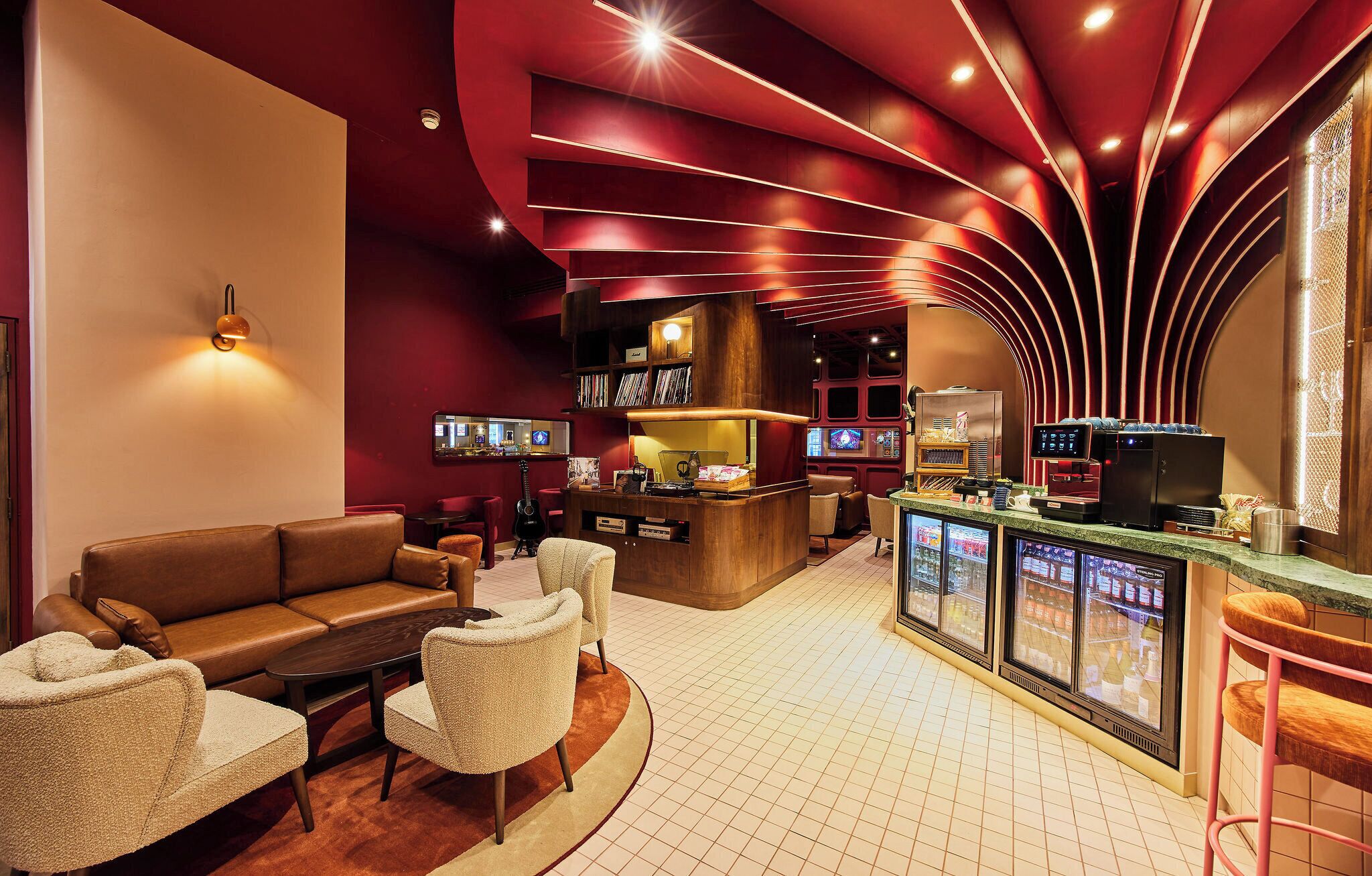 A modern bar area with a curved ceiling, a sofa, chairs, a coffee machine, and a TV screen.