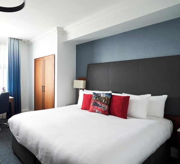 Ett hotellrum med en stor säng, en garderob i trä, ett skrivbord och en stol.
