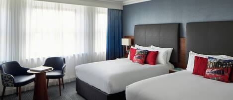 A hotel room with two beds, a desk, a chair, and a large window with curtains.