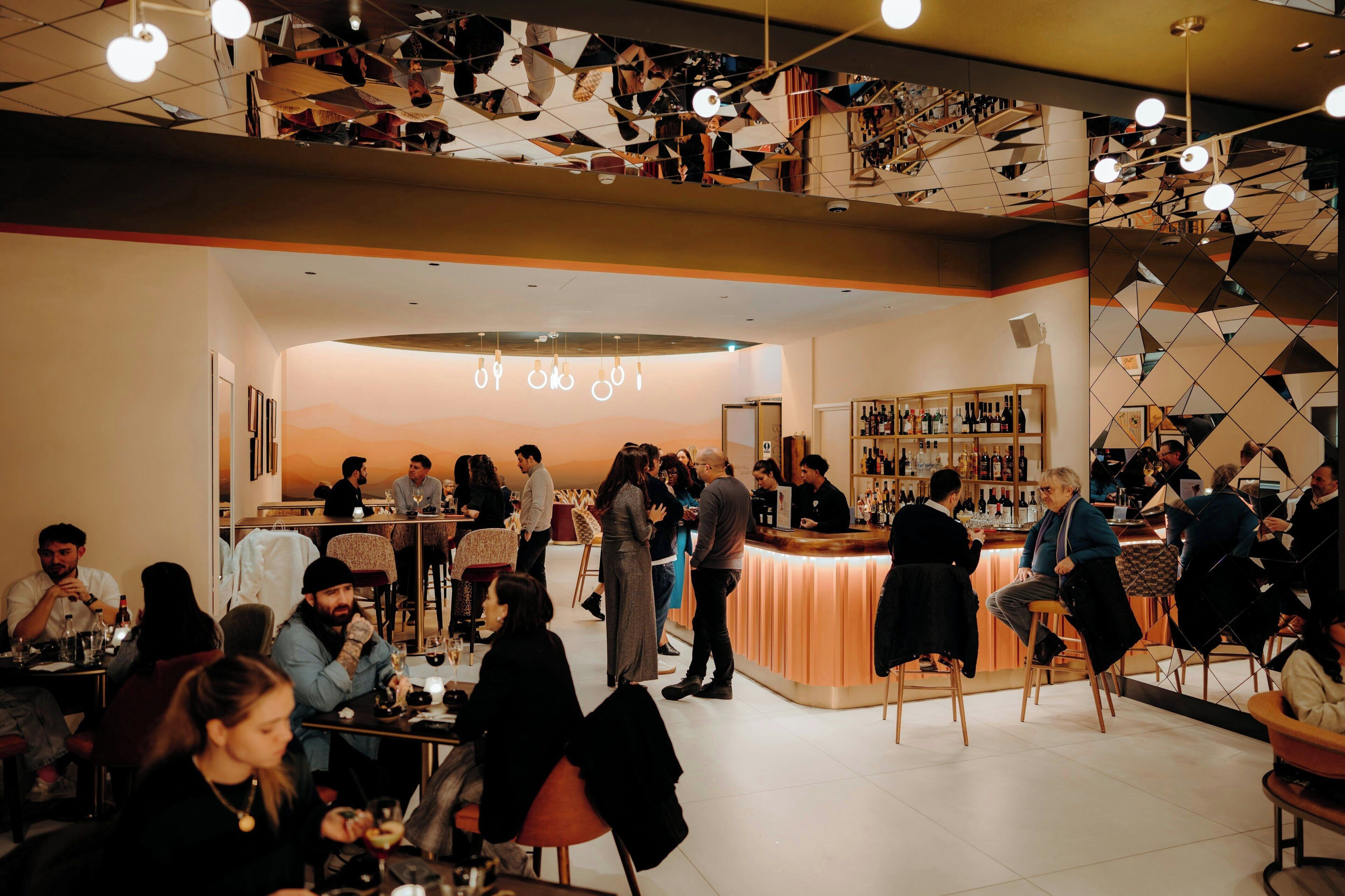 Eine Bar mit Theke, Sitzgelegenheiten und vielen Gästen.