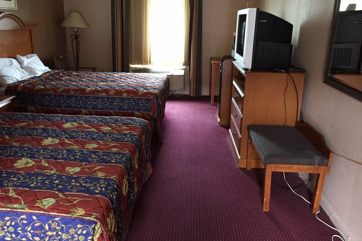 A hotel room with two beds, a television, a desk, and a chair.