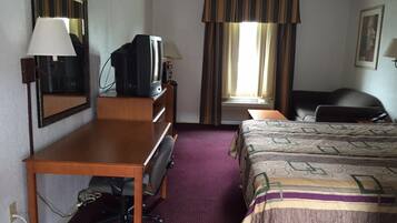 A hotel room with a bed, a desk with a chair, a television, a mirror, and a window with curtains.