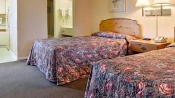 A hotel room with two beds, a nightstand, a lamp, and a painting on the wall.
