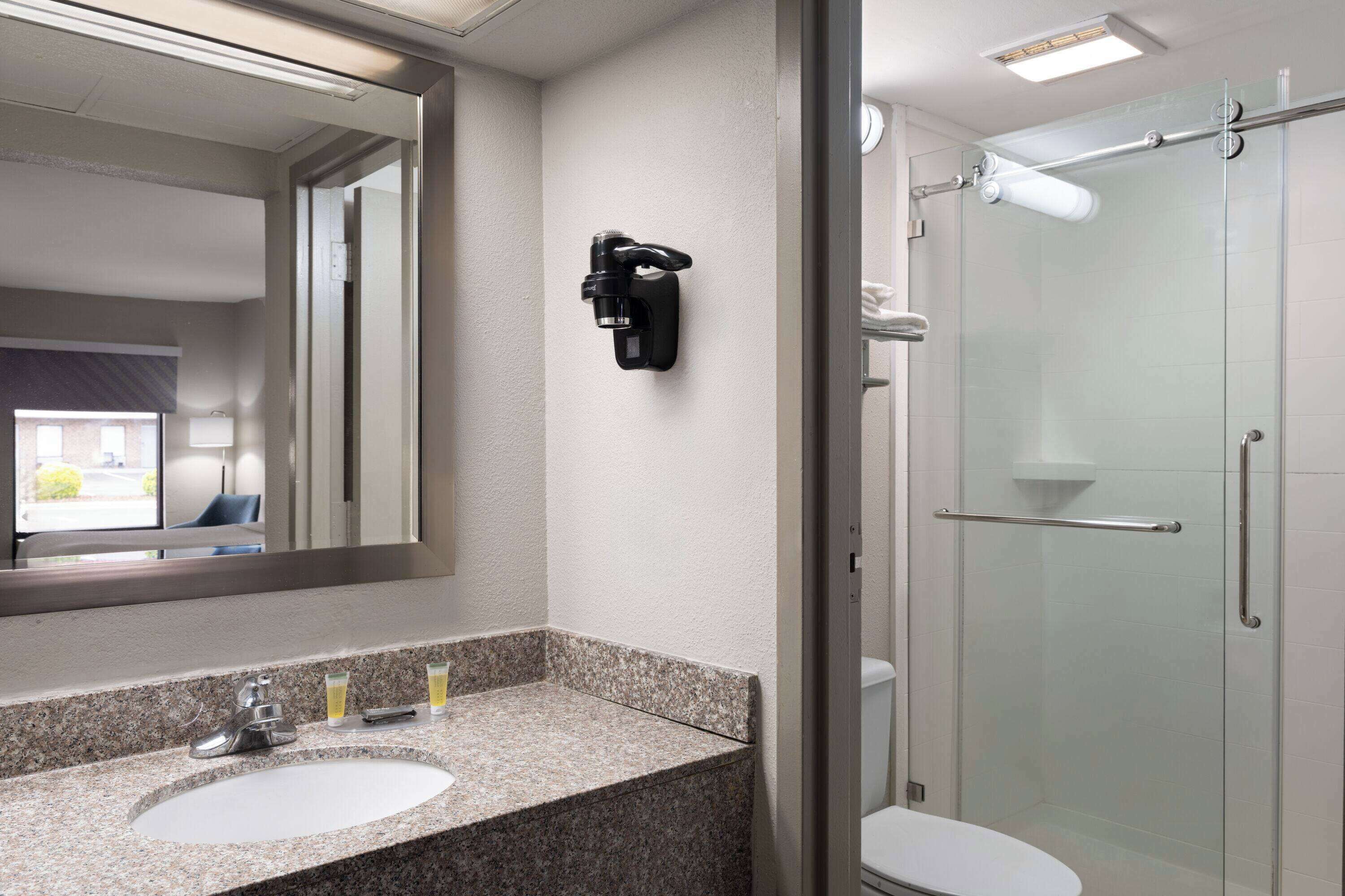 A bathroom with a granite countertop sink, a mirror, a handheld showerhead, and a glass-enclosed shower.