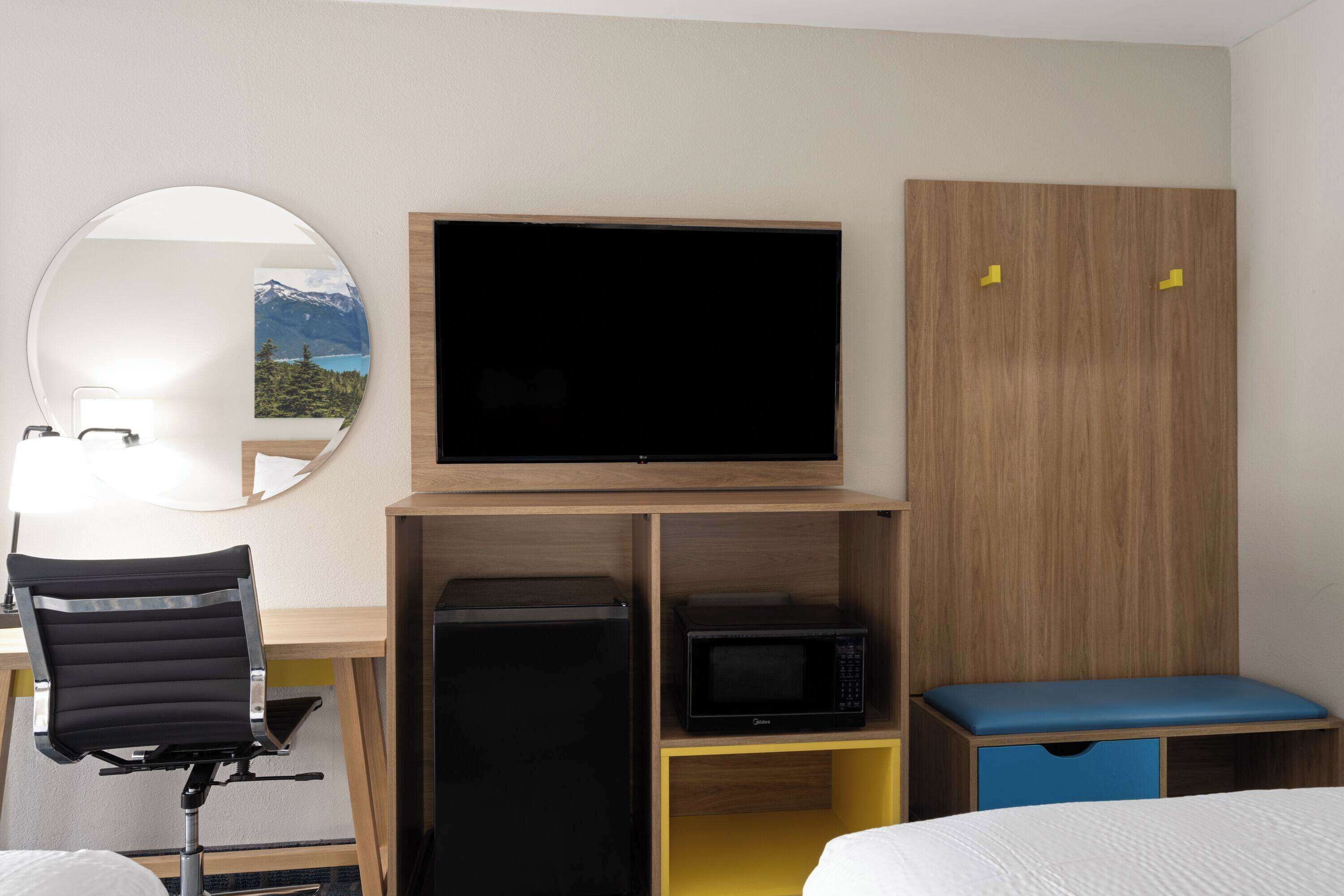 Camera d'albergo con un letto, una scrivania con sedia, una televisione, un forno a microonde e un armadio.