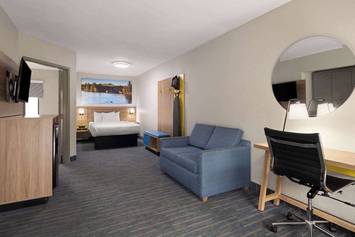 Hotelkamer met een bed, een bureau, een stoel, een bank, een televisie, een spiegel en een schilderij aan de muur.