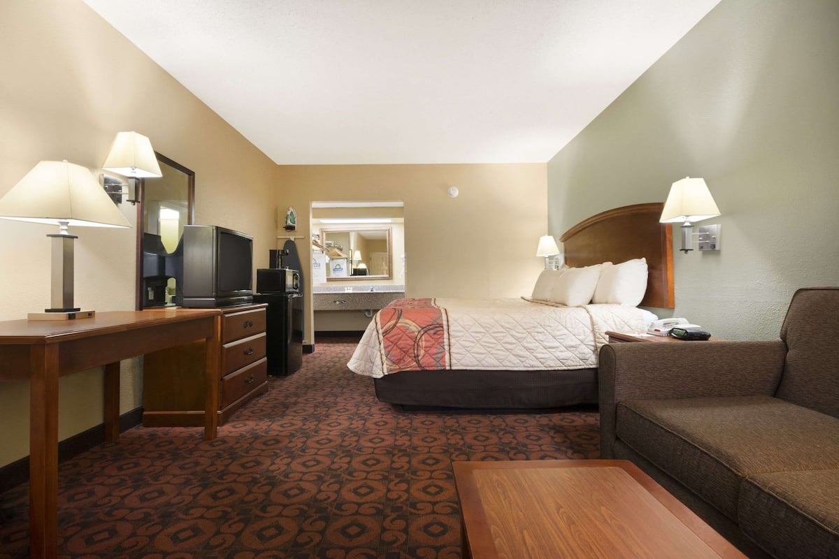 Een hotelkamer met een bed, een bank, een bureau, een televisie en een spiegel.