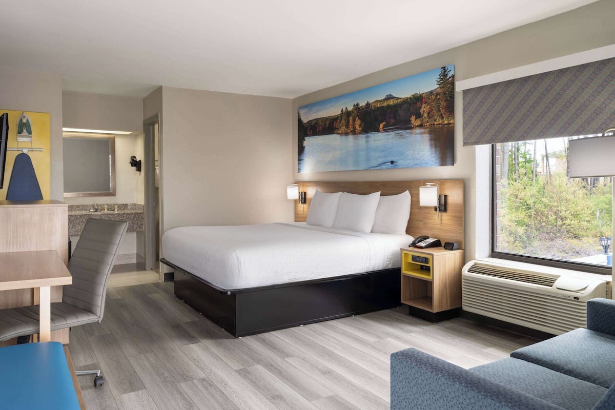 Een hotelkamer met een bed, een bureau, een stoel, een nachtkastje en een raam met uitzicht op een meer en bomen.