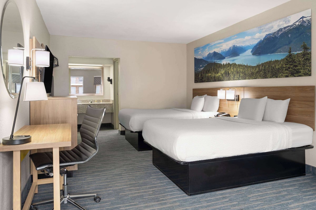 Hotelkamer met twee bedden, een bureau, een stoel, een groot raam met uitzicht op de bergen en een schilderij aan de muur.