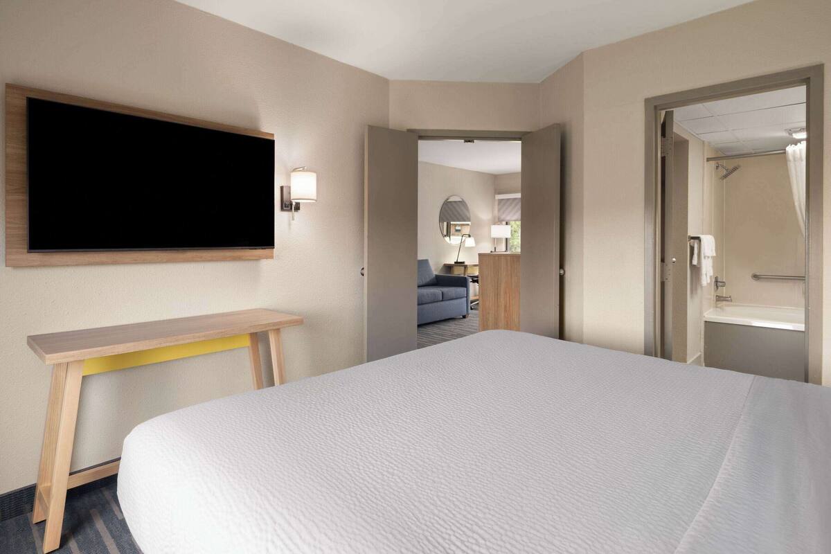Een hotelkamer met een groot bed, een aan de muur bevestigde televisie, een bureau en een badkamer zichtbaar door een geopende deur.