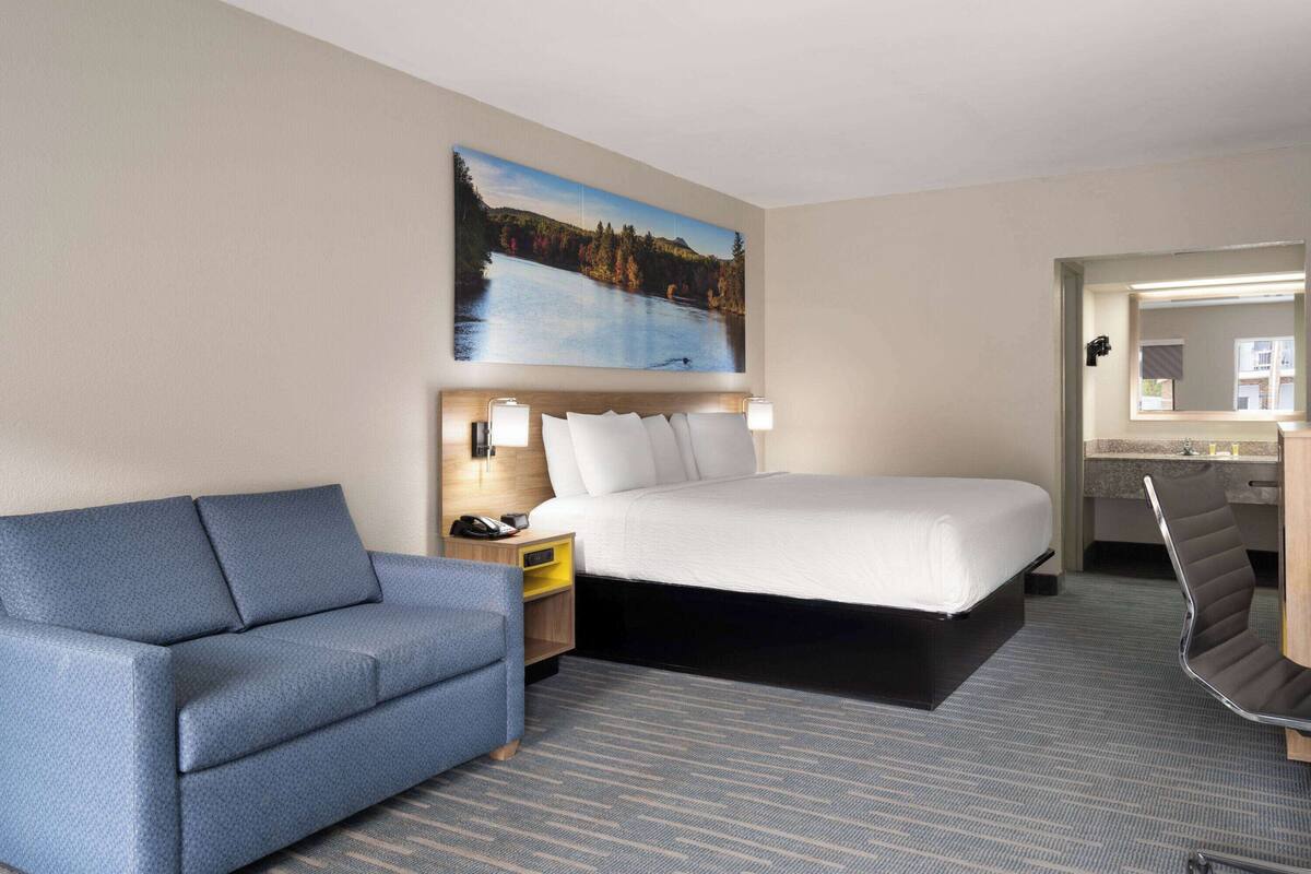 Een hotelkamer met een bed, een slaapbank, een bureau met stoel, een nachtkastje en een schilderij van een meer.