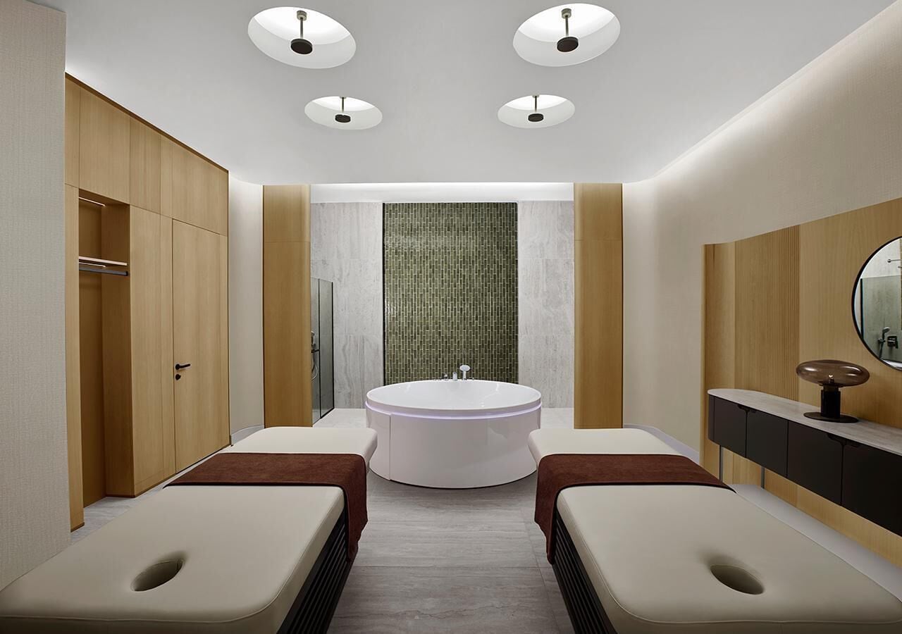 Ein modernes Badezimmer mit einer freistehenden Badewanne, zwei Massagetischen, einem Waschtisch mit Spiegel und Einbaustrahler.