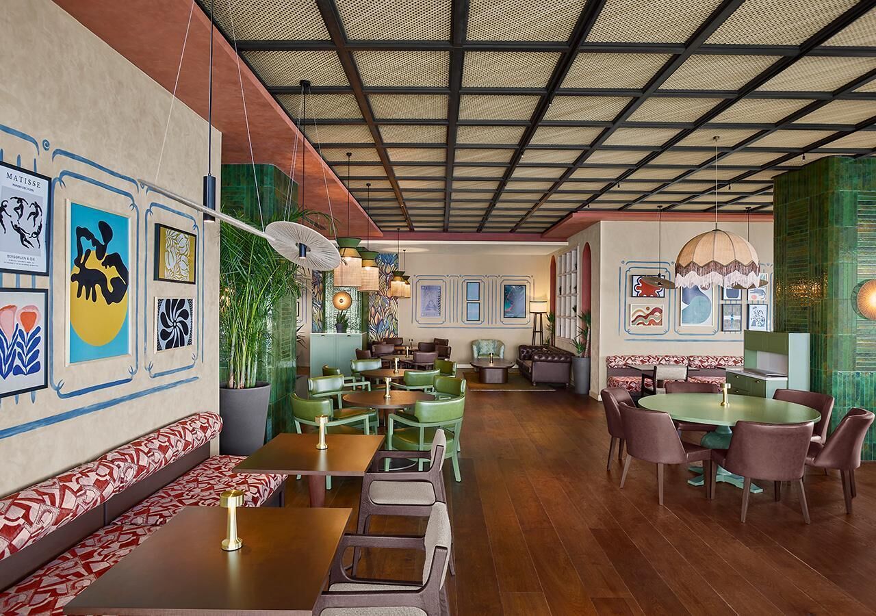 A restaurant with a high ceiling, green and brown seating, and artwork on the walls.