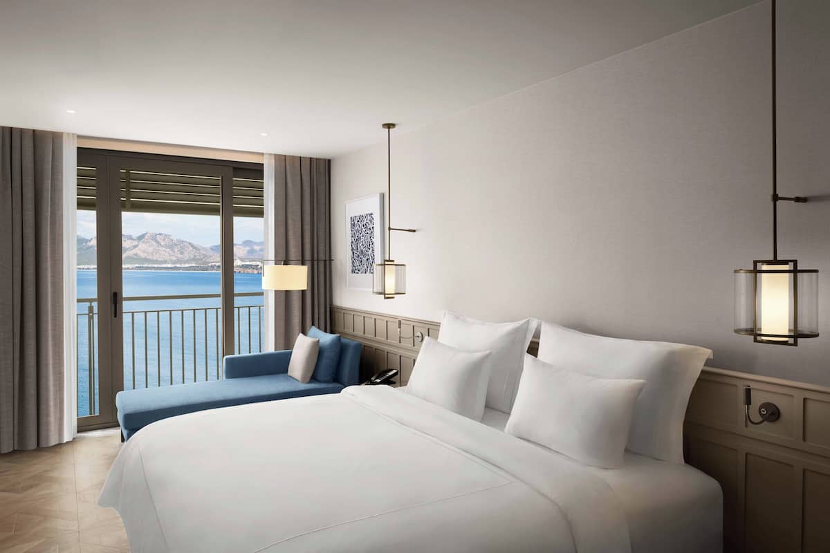 A hotel room with a large bed, a blue sofa, a view of the sea, and a balcony.