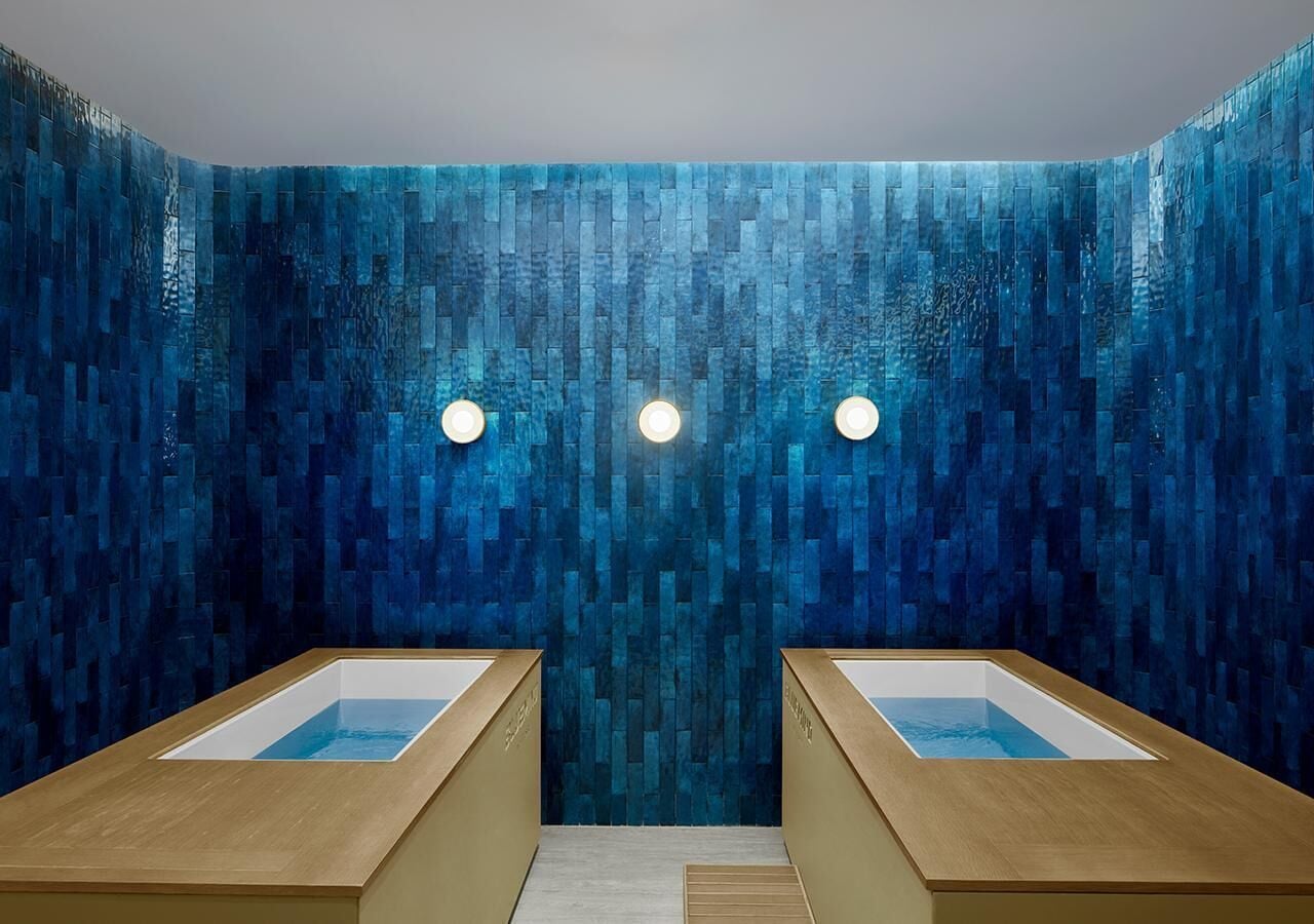 Ein Wellnessraum mit zwei Holzbadebottichen, einer strukturierten blauen Wand und drei runden Leuchten.
