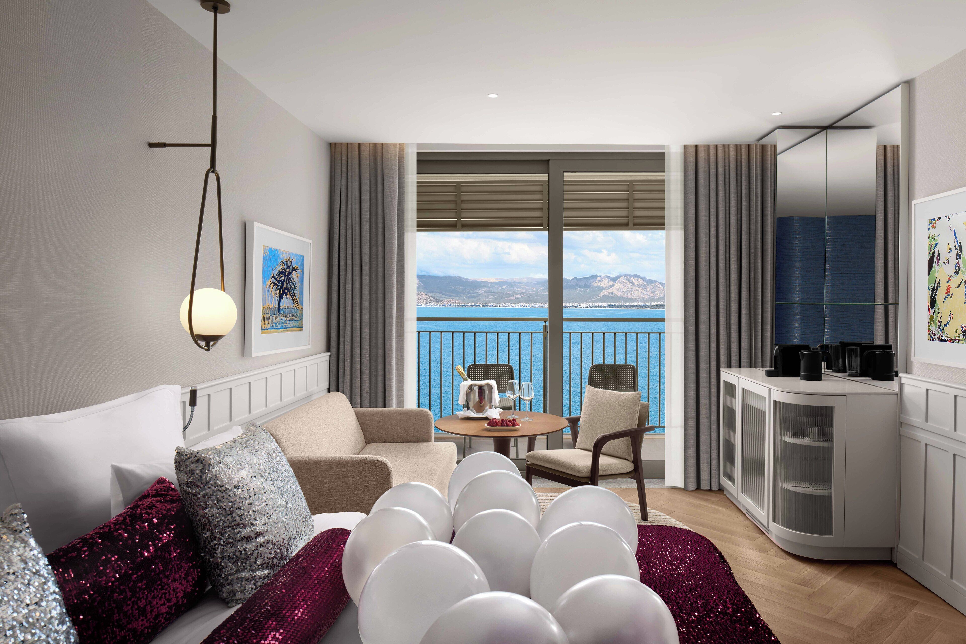 A modern hotel room with a balcony, a dining area, and a kitchen.