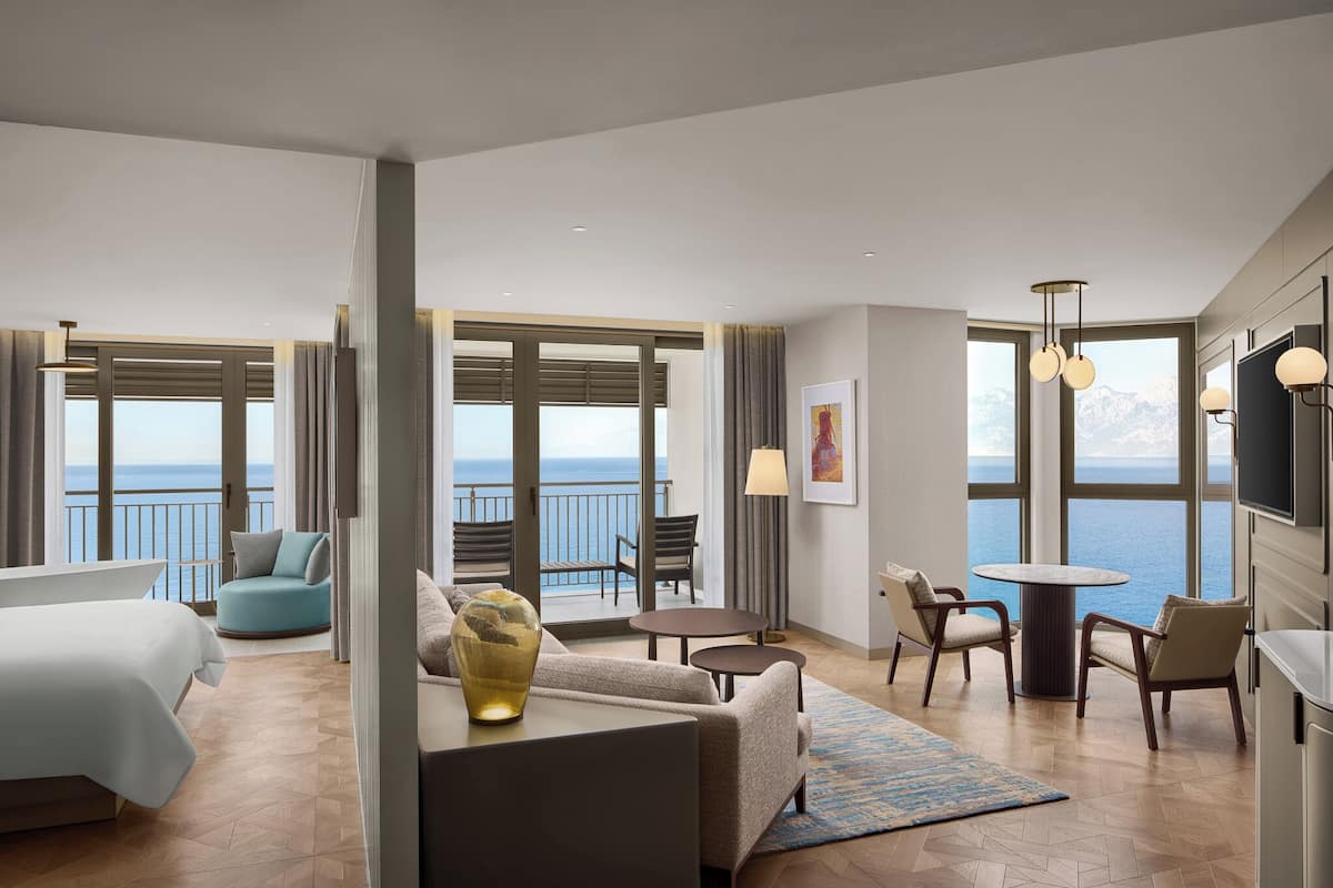 A hotel room with a bed, a sofa, a coffee table, and a view of the sea.