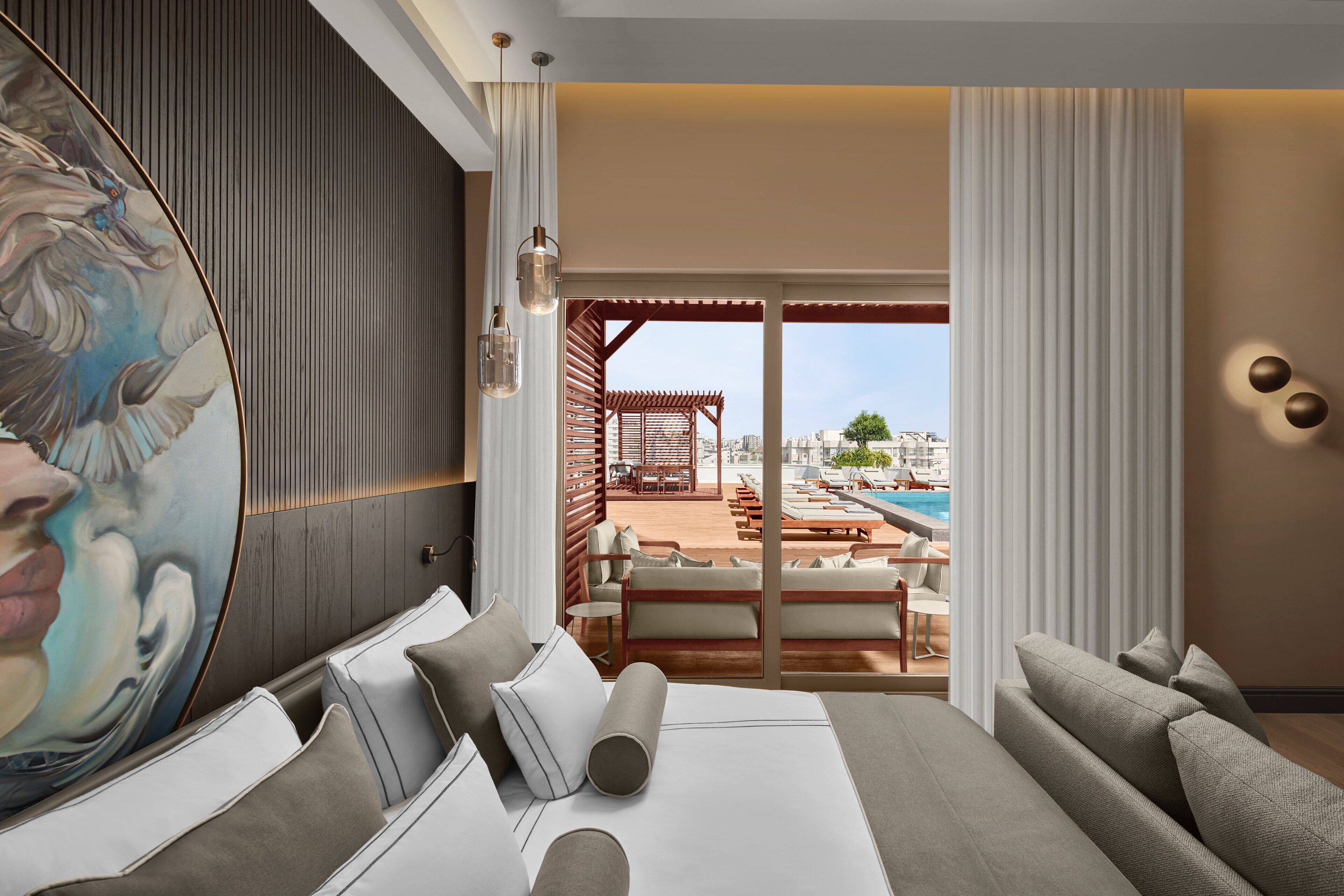 Ein Hotelzimmer mit einem großen Bett, einem Gemälde, Blick auf ein Schwimmbad und Sitzgelegenheiten sowie einer Holzpergola.