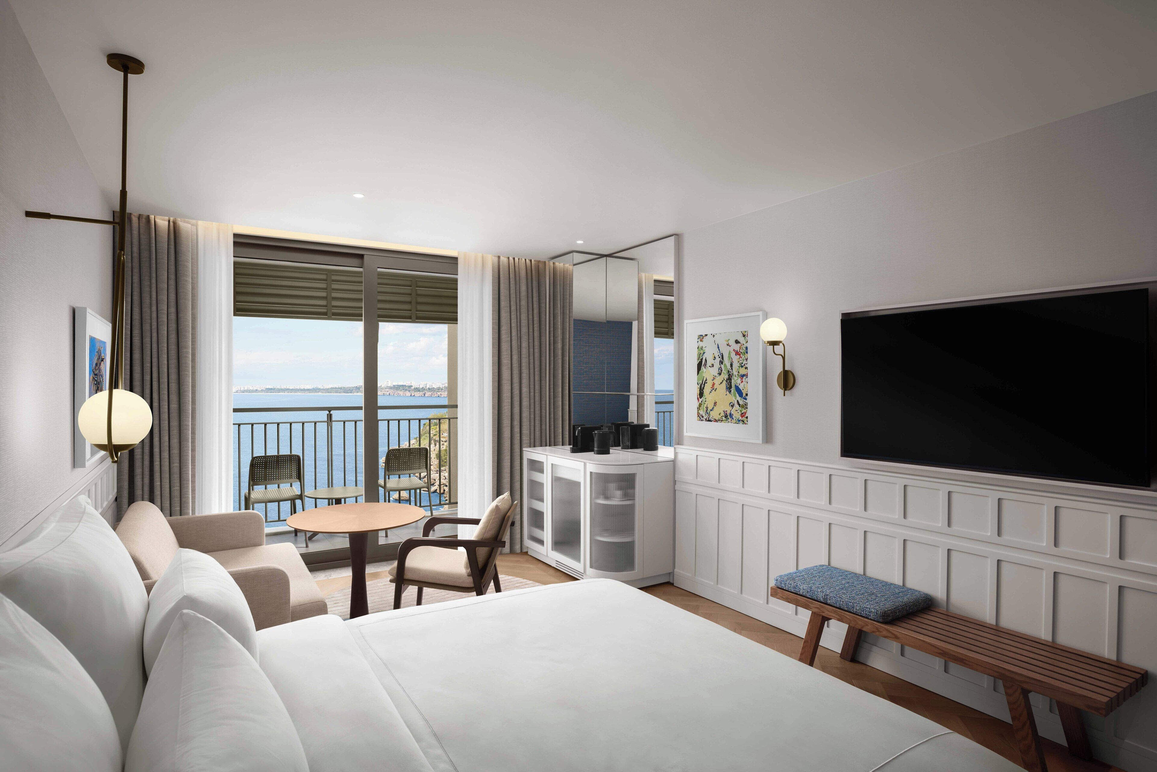 Habitación de hotel con una cama grande, un área de estar con mesa y sillas, televisión y un balcón con vistas.