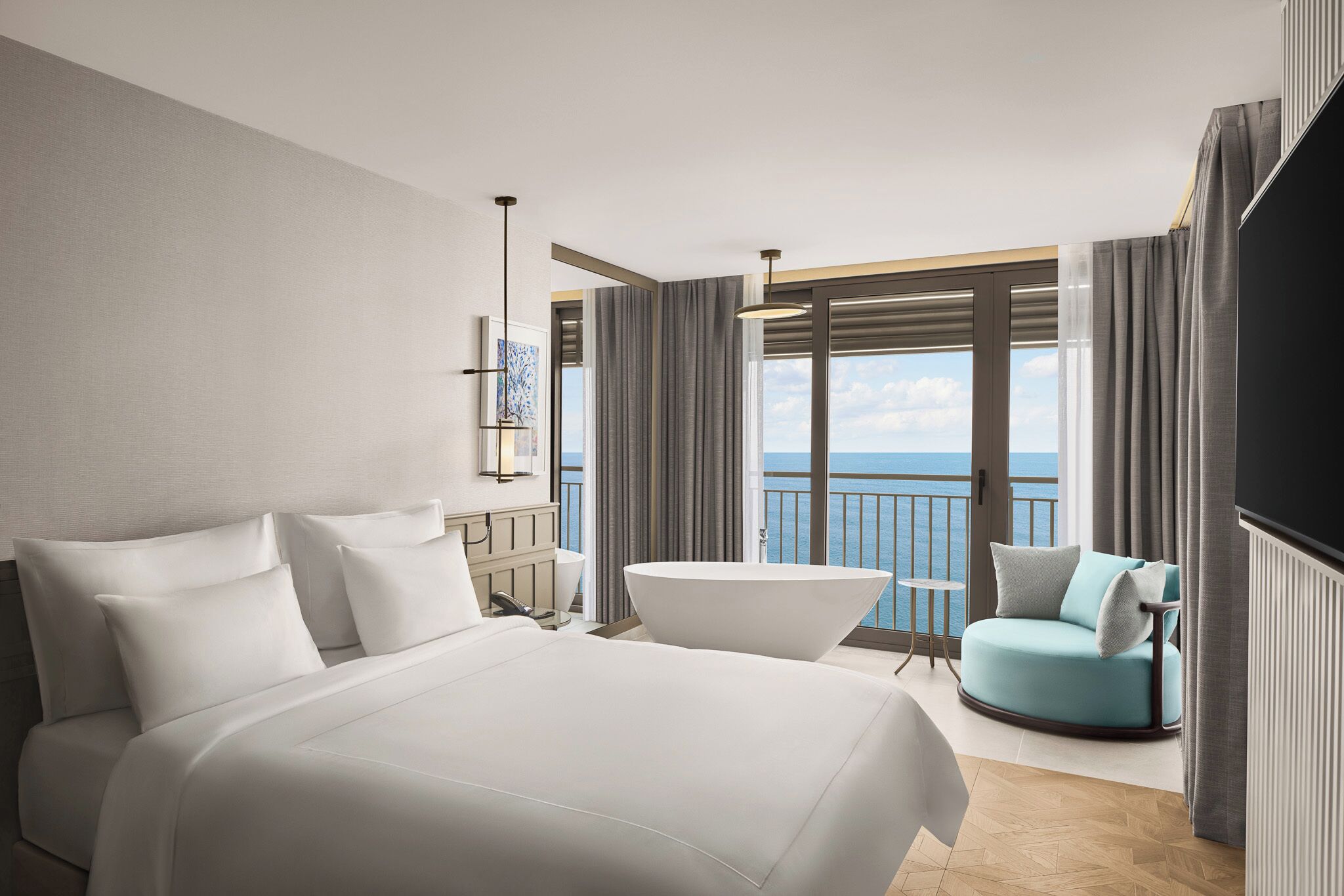 Une chambre d’hôtel moderne dotée d’un grand lit, d’un coin salon avec vue sur la mer et d’un balcon avec des rideaux.
