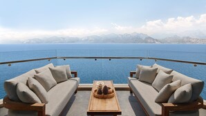 A balcony with a sofa and a wooden table, overlooking a body of water and mountains. - Akra Antalya (Antalya)