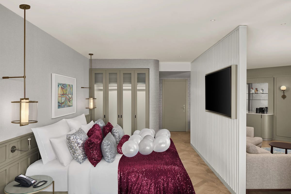 A modern hotel room with a large bed, a TV, a desk, and a seating area.