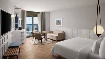 Habitación de hotel con cama, escritorio, silla, televisor y vista al mar.