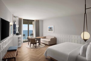 Habitación de hotel con cama, escritorio, silla, televisor y vista al mar.